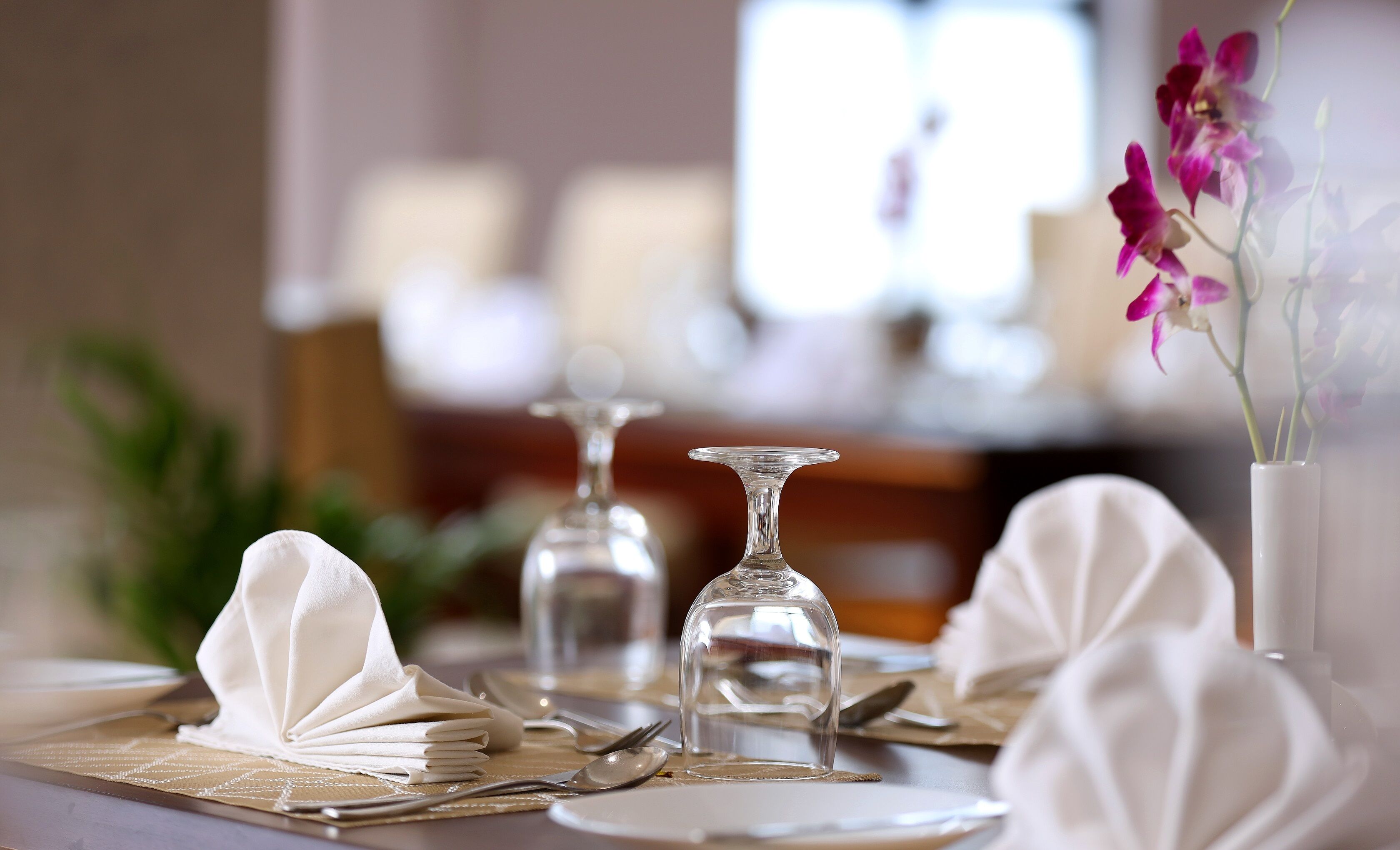 A dining table set with white napkins, cutlery, and a vase with flowers.