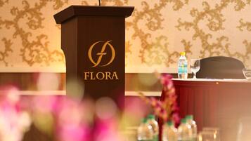 Un atril de madera con un logotipo y la palabra "FLORA", un micrófono, una botella de agua y un vaso sobre una mesa.