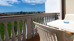 Un balcón con barandilla blanca, una mesa y sillas, con vistas a un paisaje costero con edificios y árboles.