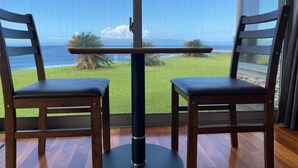 A room with two wooden chairs and a table, large windows with a view of a grassy area and the ocean. - Resort villa miko (Oshima)