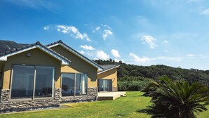 A modern house with large sliding glass doors, a stone foundation, and a well-maintained lawn. - Resort villa miko (Oshima)