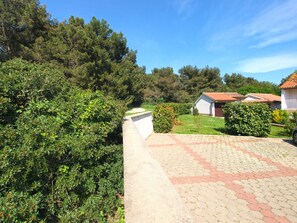 Set amidst lush greenery, this charming property features a paved driveway leading to a white building with a red-tiled roof.