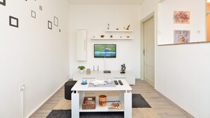 Un soggiorno moderno con una TV a schermo piatto montata a parete, un mobile bianco, un tavolino con oggetti decorativi e un poggiapiedi nero.