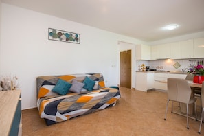 A modern living room with a sofa, a dining table, and a kitchen area.
