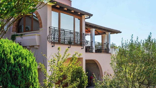 Un edificio de dos pisos con balcón, ventanas de arco y un jardín.