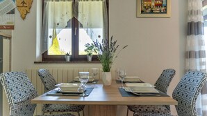 Un comedor con una mesa de madera dispuesta para dos personas, sillas con estampado, una planta en maceta y un cuadro en la pared.
