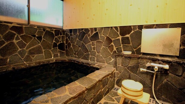 A stone-walled hot tub with a wooden stool and a towel rack.