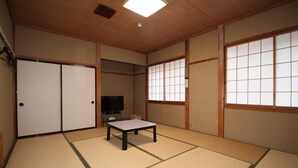 A traditional Japanese room with tatami flooring, sliding doors, a television, and a small table.