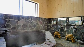 A stone-walled bathroom with a hot tub, wooden stools, and a window.