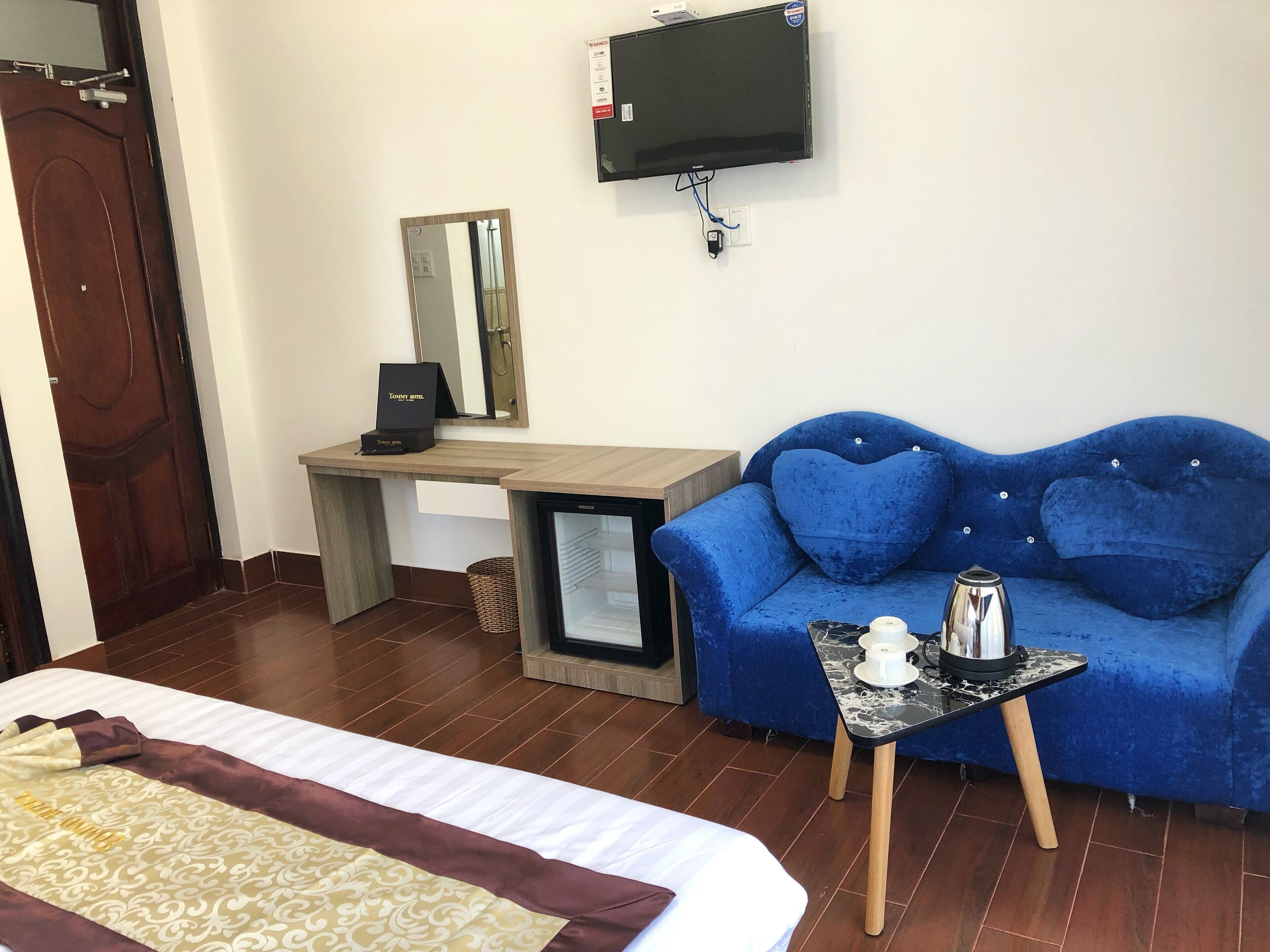 Ein Hotelzimmer mit einem Bett, einem blauen Sofa, einem kleinen Tisch mit Kaffeemaschine, einem an der Wand montierten Fernseher und einem Schreibtisch mit Spiegel.
