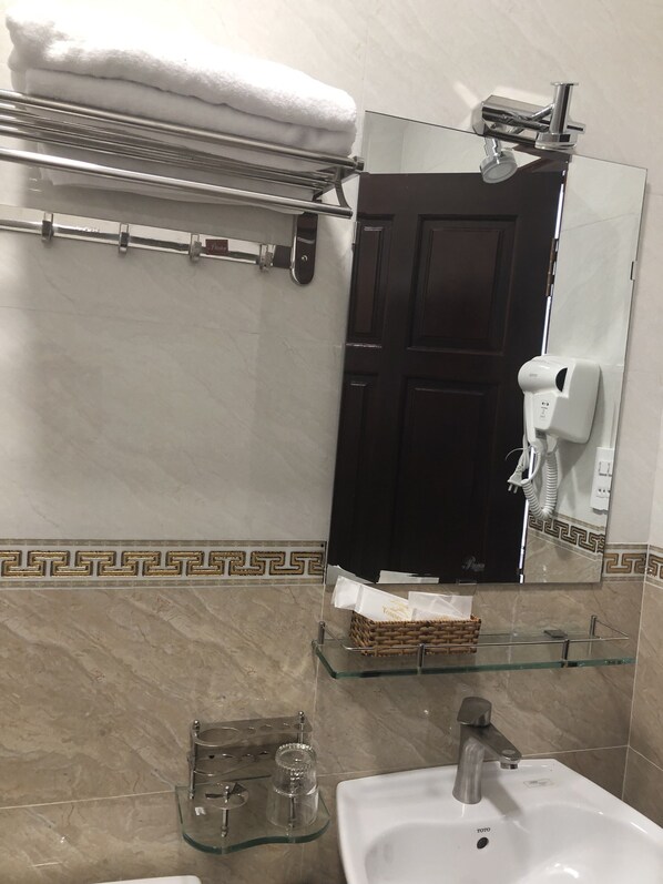 A bathroom with a white sink, a glass shelf, a towel rack, a hairdryer, and a door. - Tommy Hotel Dalat (Xuan Huong - Da Lat)