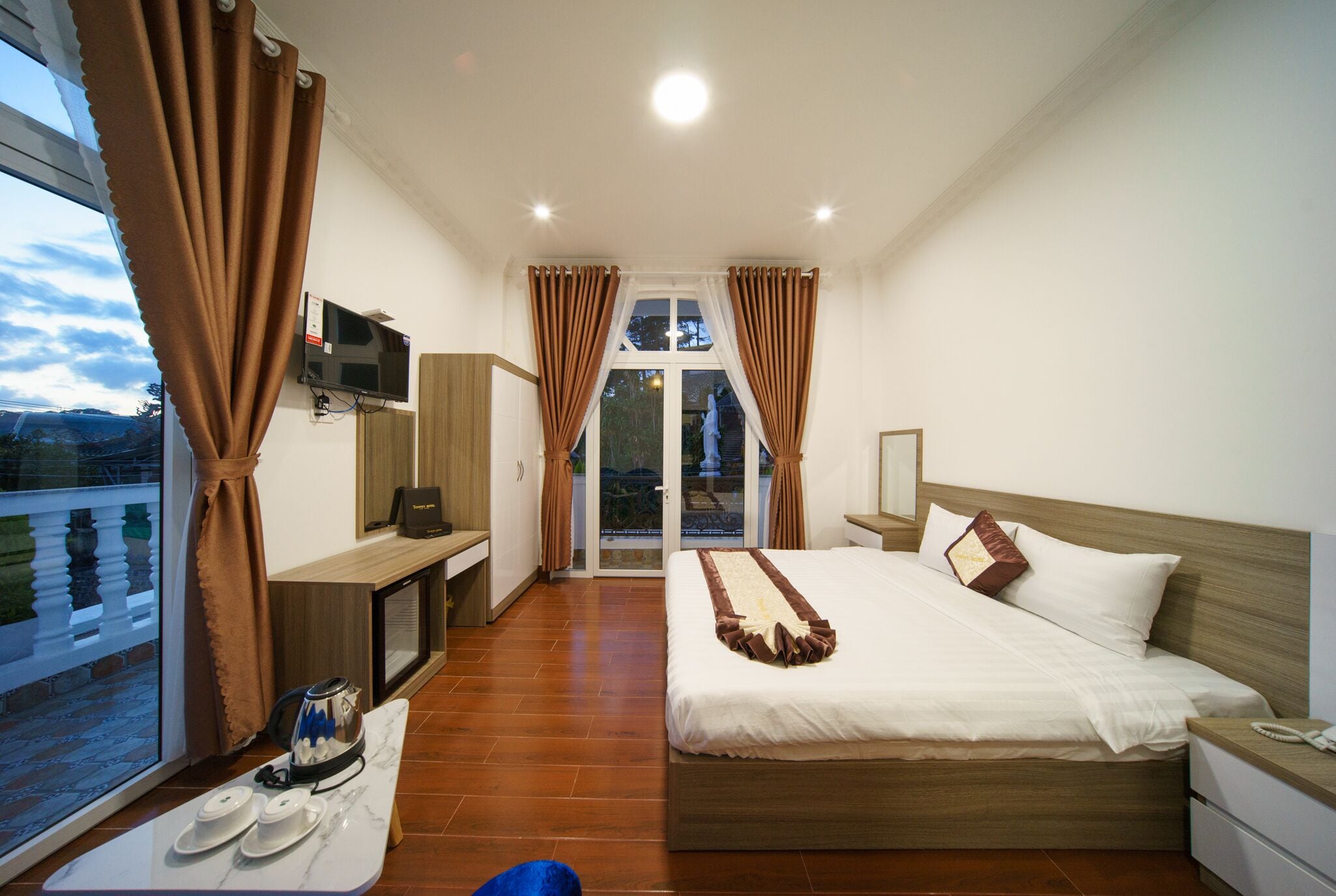 A hotel room with a bed, a desk, a TV, and a balcony with curtains.