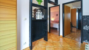 Een gang met een houten garderobe, een zwarte plank met een plant en een lantaarn, en een slaapkamer met een bed en een hartvormige decoratie.