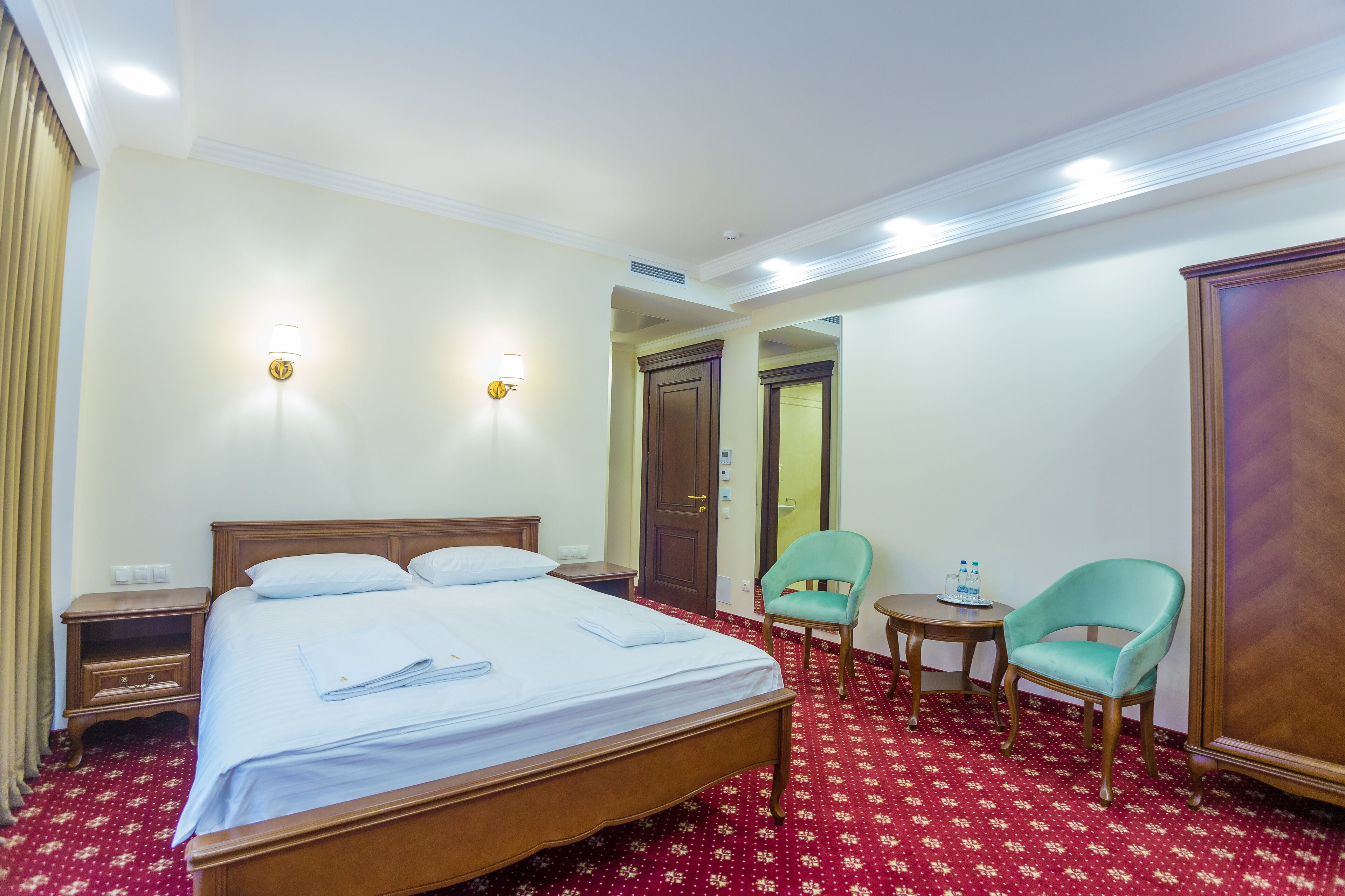 Quarto de hotel com uma cama grande, duas cadeiras, uma mesinha e um guarda-roupa.