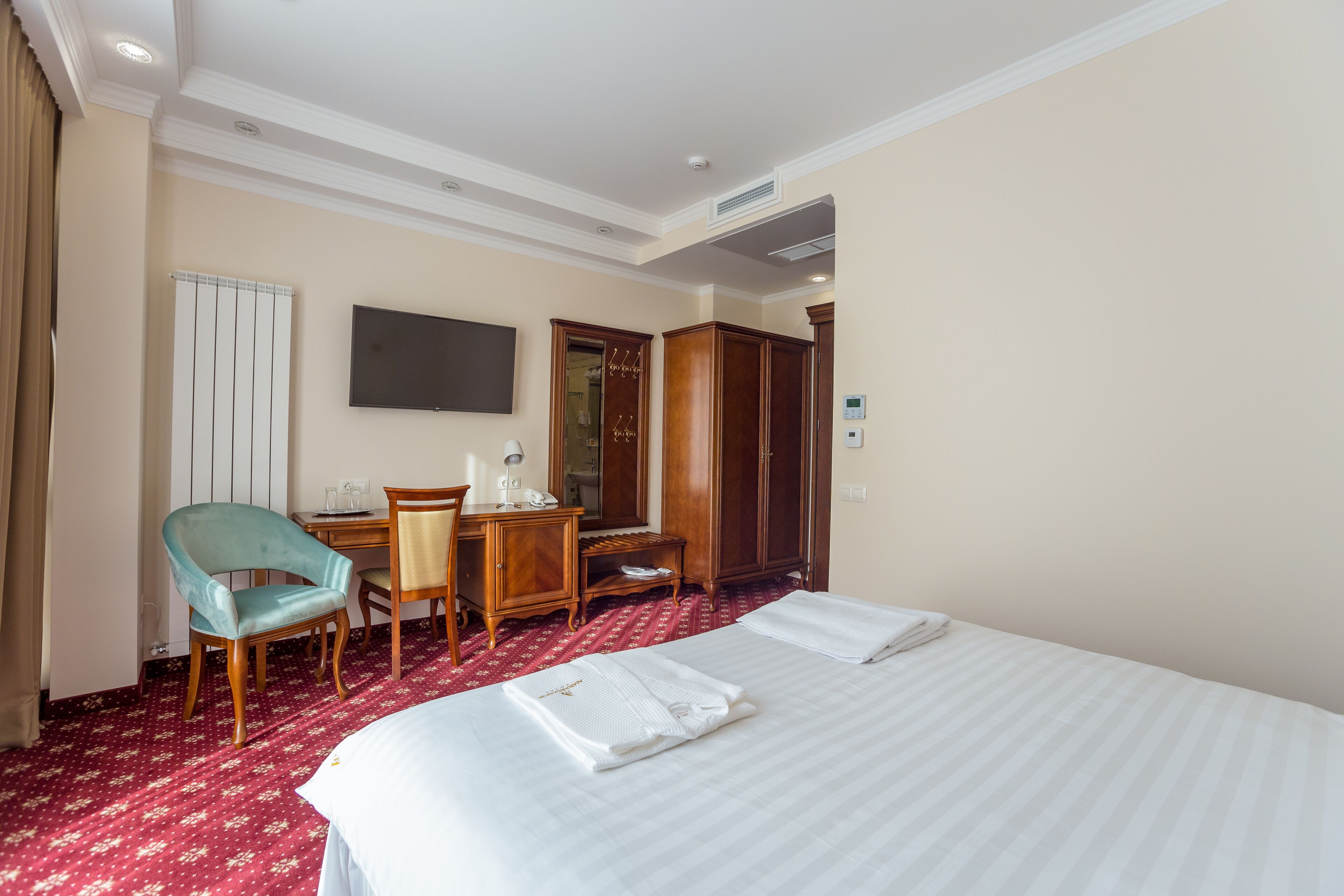 A hotel room with a large bed, a desk with a chair, a television, and a wardrobe.