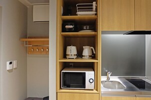 A compact kitchen with a microwave, coffee maker, and kettle on shelves, a stainless steel sink, and wooden cabinets.