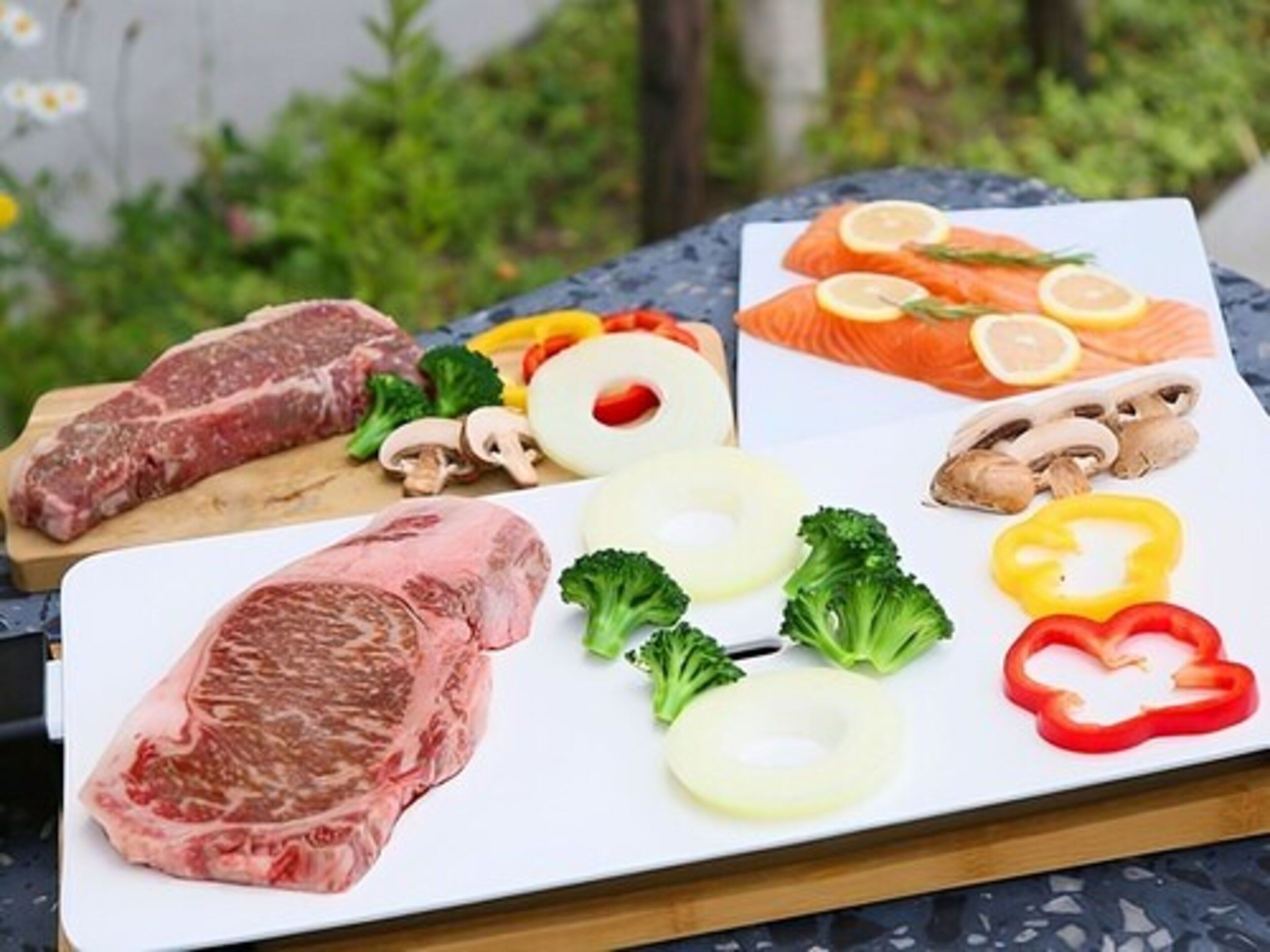 Diversas carnes crudas y verduras sobre una tabla de cortar.