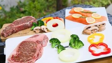 Diversas carnes crudas y verduras sobre una tabla de cortar.