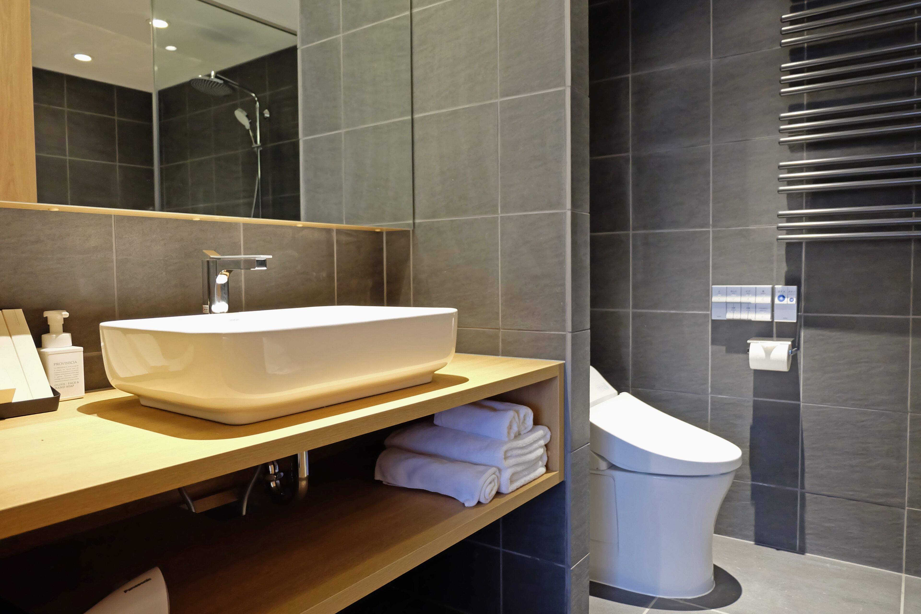 A modern bathroom with a large white sink, a mirror, a toilet, and a towel rack.