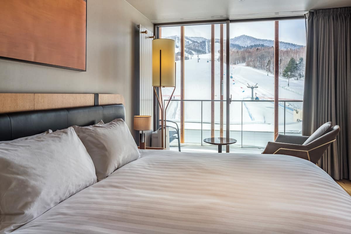 A hotel room with a large bed, a chair, a small table, and a view of a snowy mountain.
