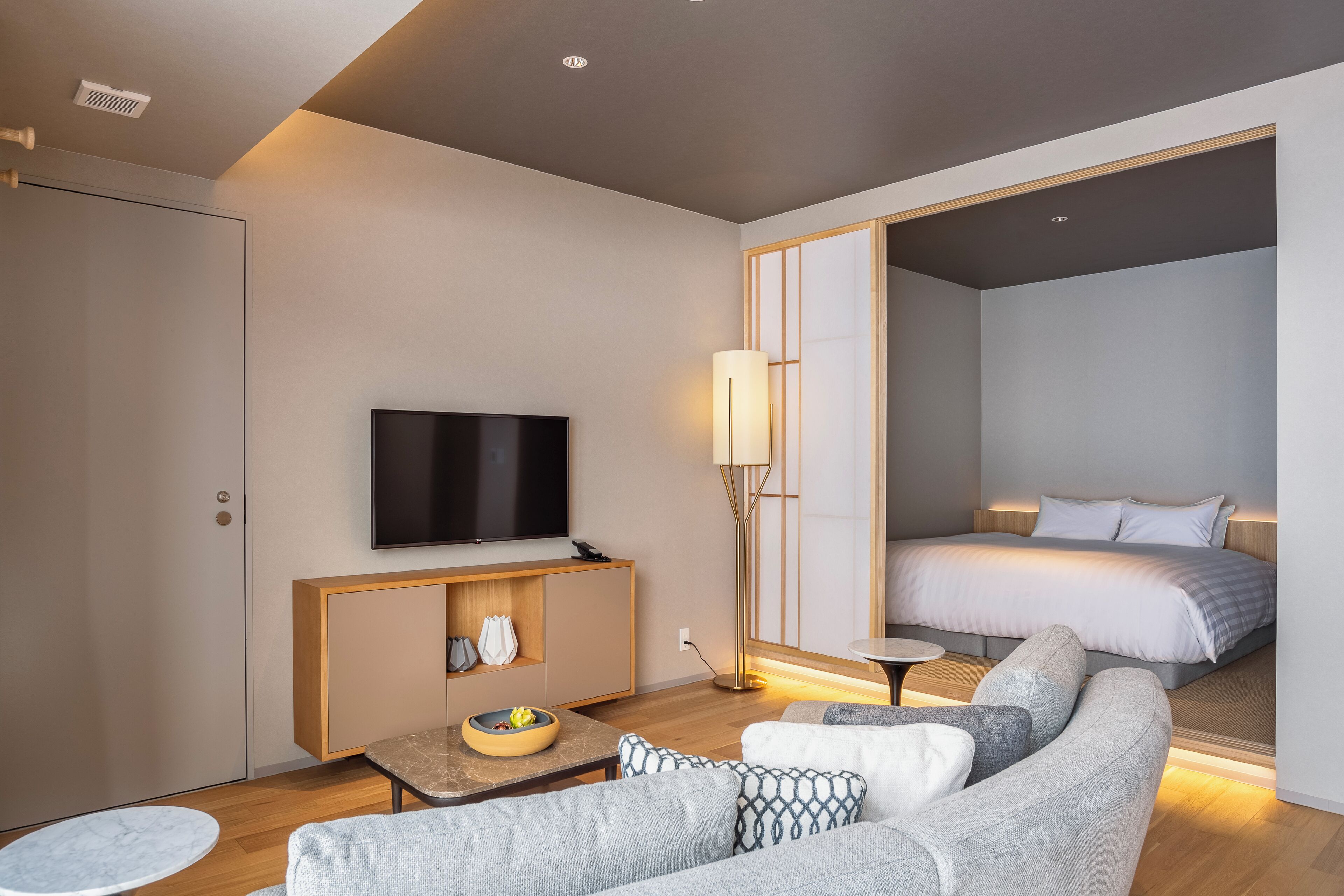 A modern hotel room with a sofa, a small table, a TV, a bedside table, and a bed.