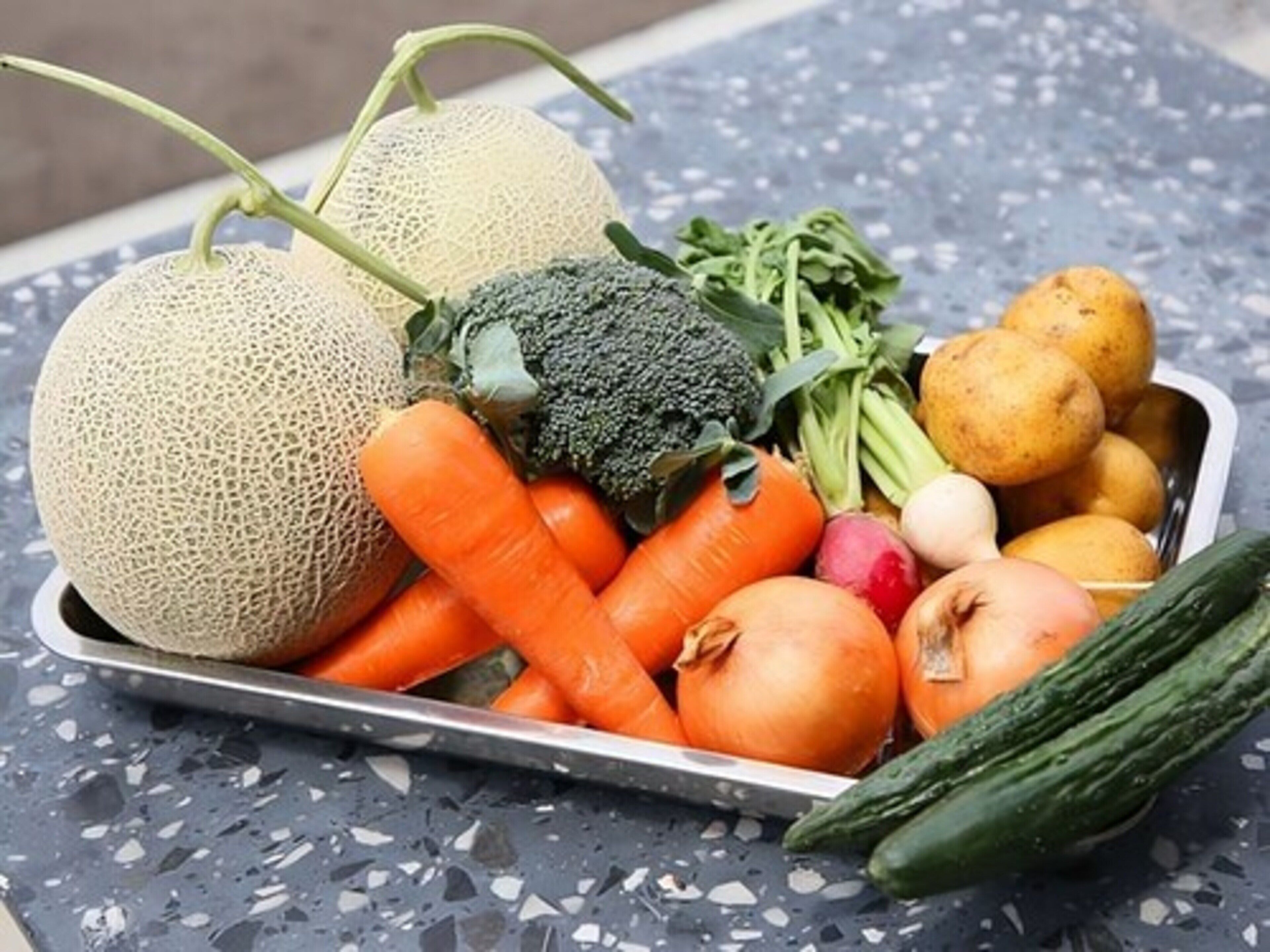 A tray of fresh vegetables including carrots, broccoli, onions, potatoes, and a cucumber.