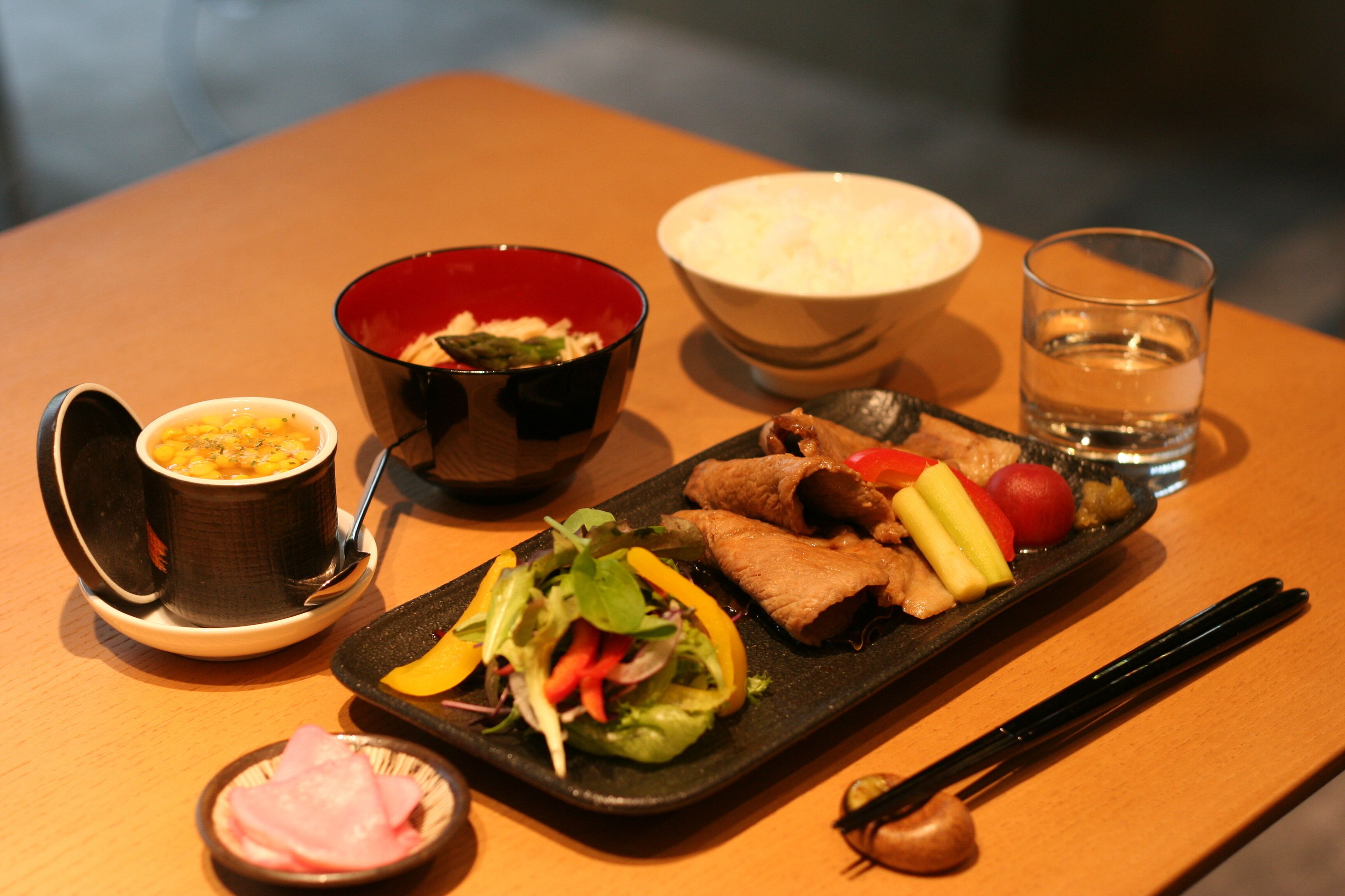 A table with a variety of dishes including a bowl of rice, a bowl of soup, a plate with vegetables and meat, and a small dish of pickled vegetables.
