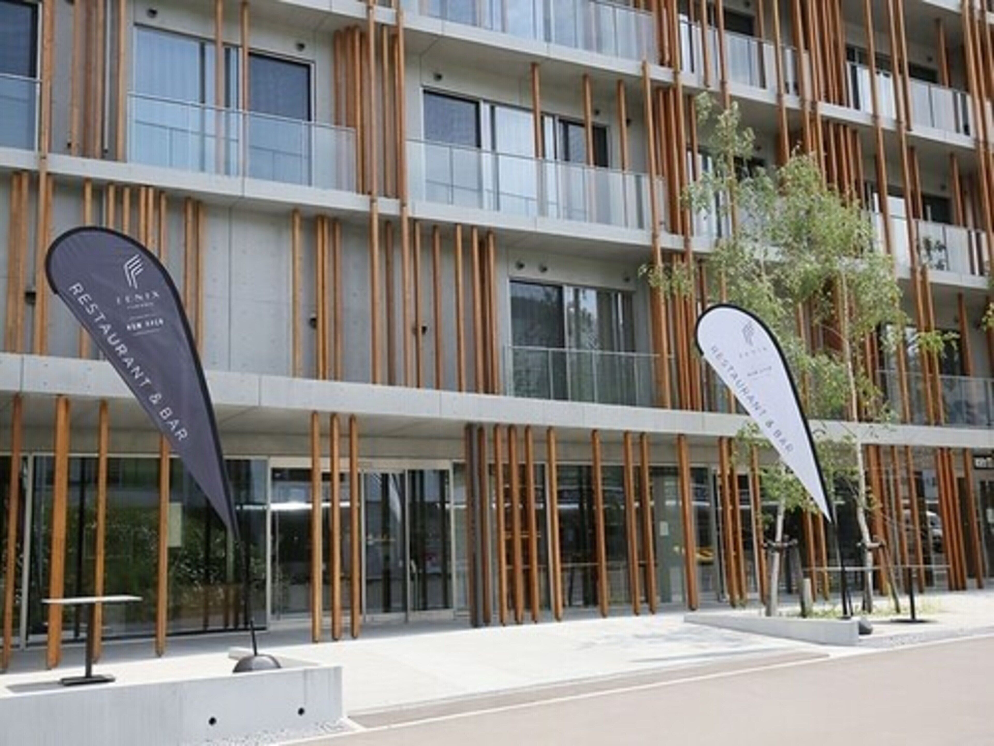 A modern building with vertical wooden slats, large windows, and two flags indicating a restaurant and bar.