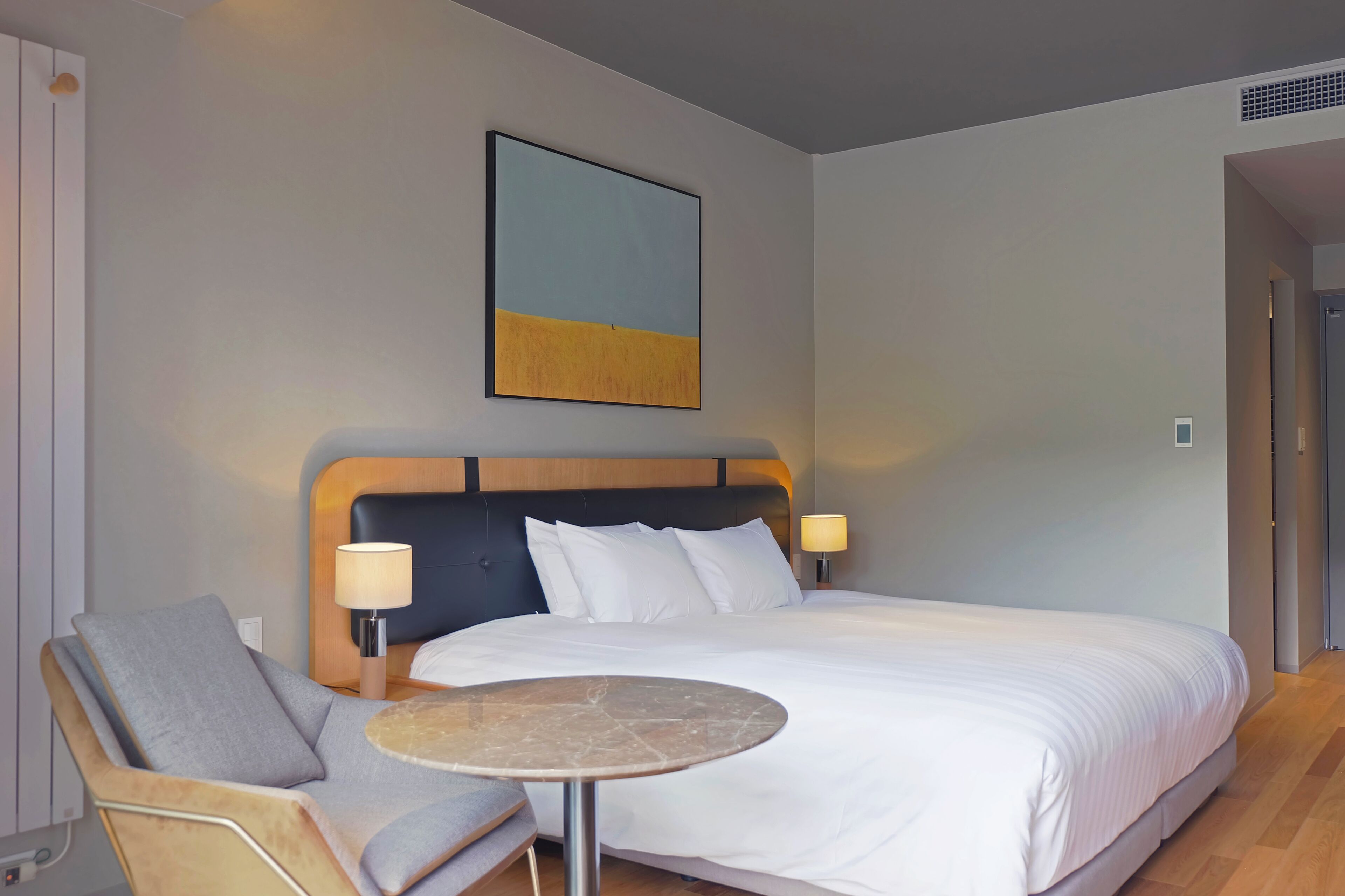 Une chambre d’hôtel avec un grand lit, une table de chevet, une chaise et une œuvre d’art accrochée au mur.