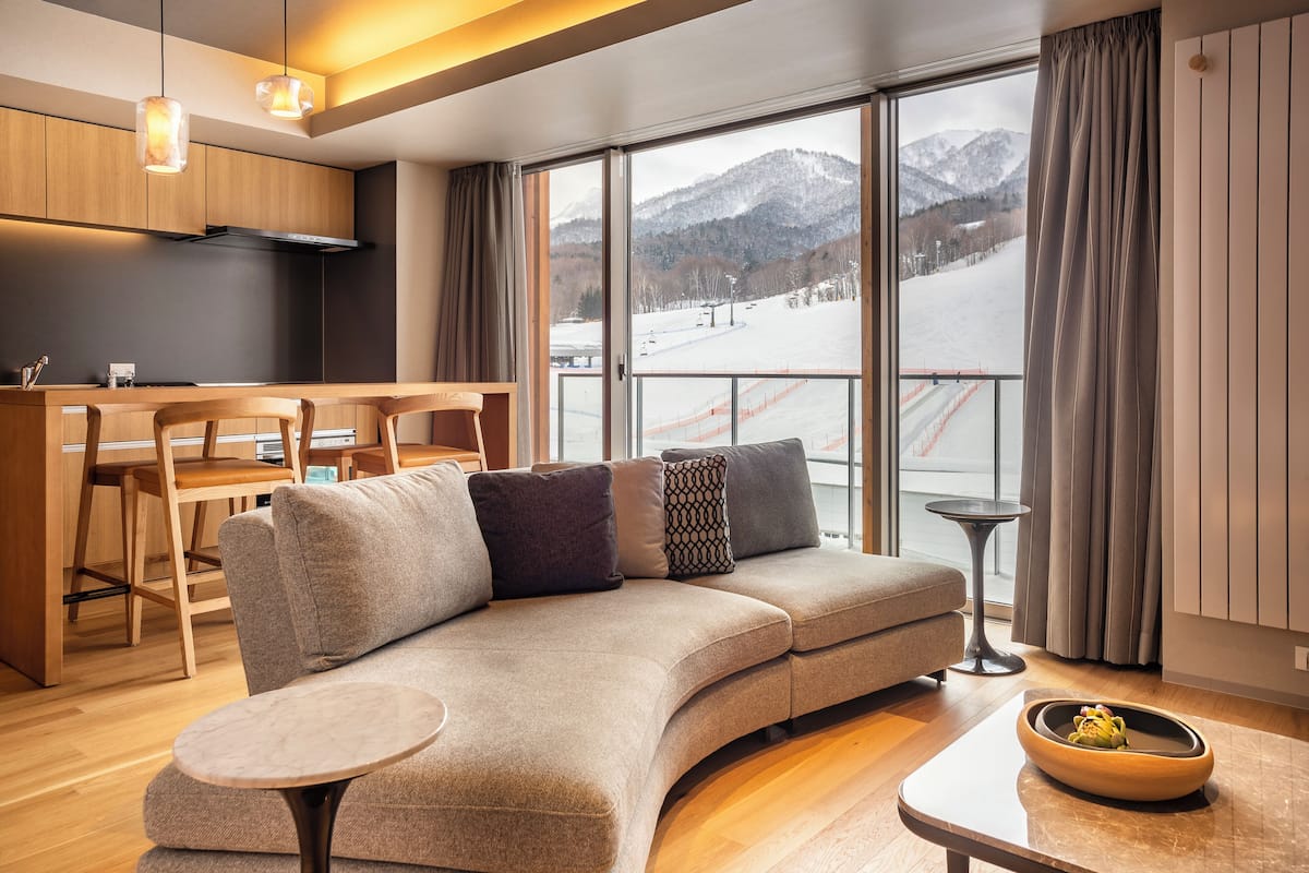 A modern living room with a sofa, a round coffee table, and a view of a snowy mountain landscape through large windows.