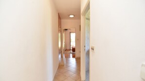 Un couloir étroit, dont le sol est recouvert de carreaux, mène à une pièce dotée d’une porte.