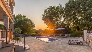 A pool area with a stone patio, lounge chairs, and a staircase leading to a building. - Holiday house VESNA with pool (Milovčići)