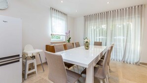 A modern dining area with a white table, beige chairs, and a vase with flowers. - Holiday house VESNA with pool (Milovčići)