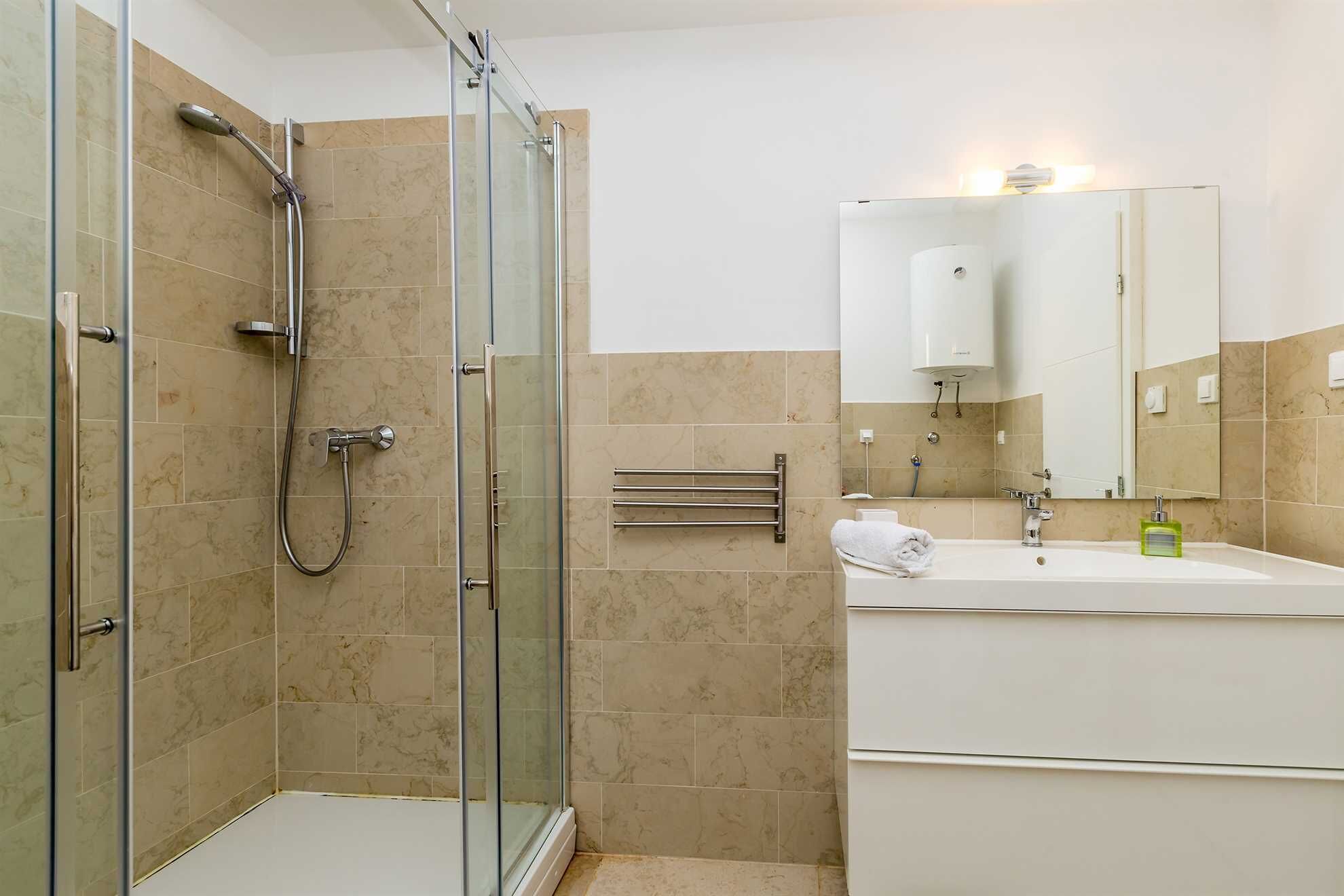 Een moderne badkamer met een douchecabine van glas, een witte wastafel en een grote spiegel.