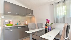 A modern kitchen with grey cabinets, a dining table with chairs, and a window with sheer curtains. - Apartment 1642/16897 (Istria - Pula), 5000m from the beach (Pula)