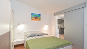 A bedroom with a bed, a nightstand, a green bedspread, a painting on the wall, and a view into the kitchen. - Apartment 1642/16897 (Istria - Pula), 5000m from the beach (Pula)
