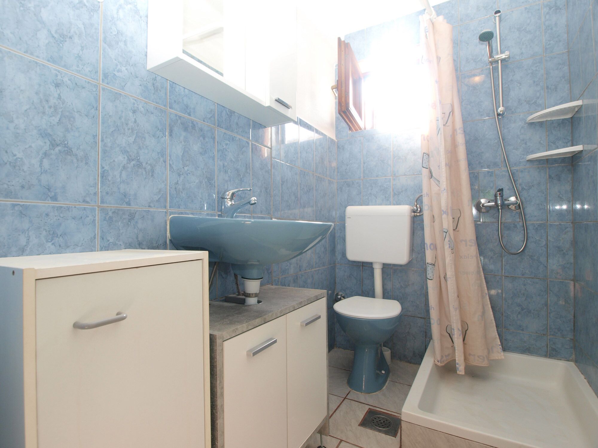 A bathroom with a sink, toilet, shower, and cabinet.