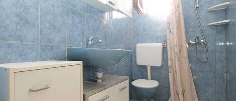 A bathroom with a sink, toilet, shower, and cabinet.