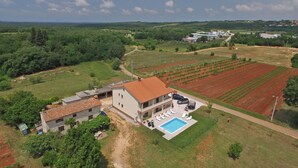Une maison à deux étages avec une piscine, entourée de champs et de verdure.
