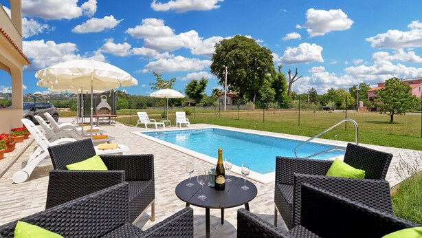 Un espace extérieur avec une piscine, des chaises longues, une table avec une bouteille et des verres, et des parasols.