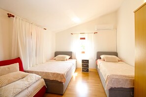 A bedroom with two beds, a red couch, a wooden floor, and an air conditioning unit.