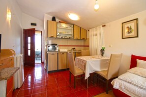 Una cocina compacta con microondas, una mesa de comedor con sillas y piso de baldosas rojas.