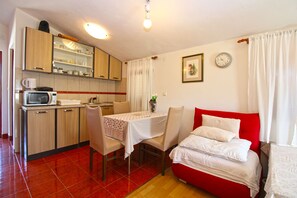 A compact room with a kitchenette, a dining table, a bed, and a clock on the wall.