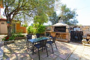 Une terrasse extérieure avec un four à pizza en pierre, deux chaises et une table.