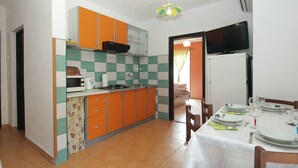 A compact kitchen with orange cabinets, a microwave, and a gas stove. There is a dining area with a table set for two, and a TV mounted on the wall. - Apartment 1676/17366 (Istria - Banjole), 1000m from the beach (Banjole)