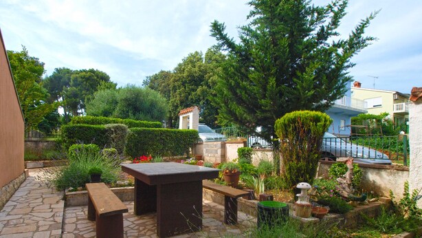 A patio with stone flooring, a wooden table, and benches. There are potted plants and a small garden area with various shrubs and flowers. - Apartment 1676/17366 (Istria - Banjole), 1000m from the beach (Banjole)
