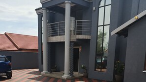 Un edificio con vestíbulo cubierto, camino de entrada pavimentado y un coche azul estacionado adelante.