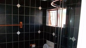 Un baño con paredes de azulejos negros, un inodoro blanco y una cabina de ducha de vidrio.