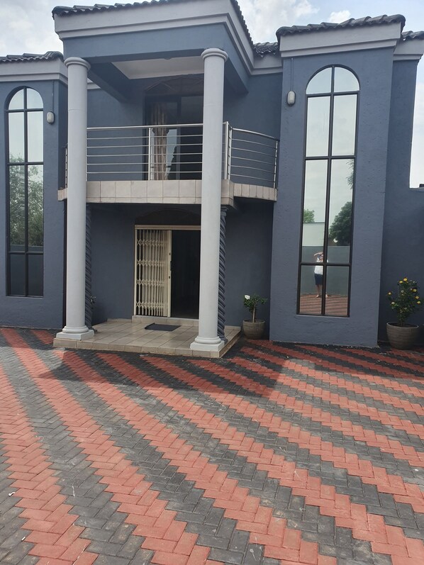 A two-story building with a balcony, large windows, and a patterned brick driveway. - Koiketla Guesthouse (Akasia)
