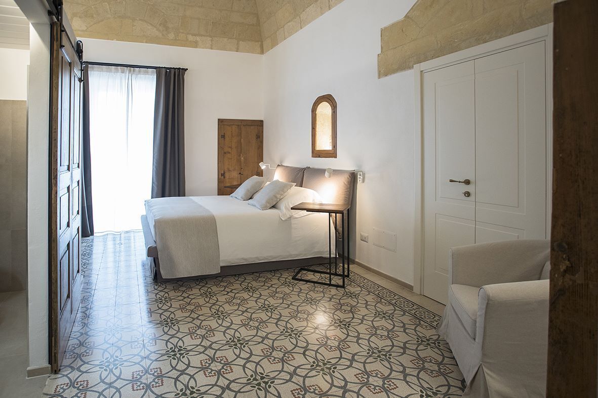 A bedroom with a bed, a bedside table with a lamp, a chair, and a door.